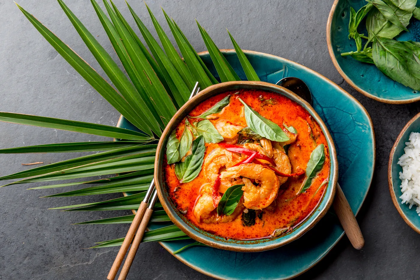 Reinhardt koch - Kochkurse und Gastronomie-Service - Rotes Curry mit Garnelen aus Thailand. Traditionelles rotes Currygericht aus Thailand mit Garnelen und Kokosmilch. Panang-Curry auf blauem Teller vor grauem Hintergrund.