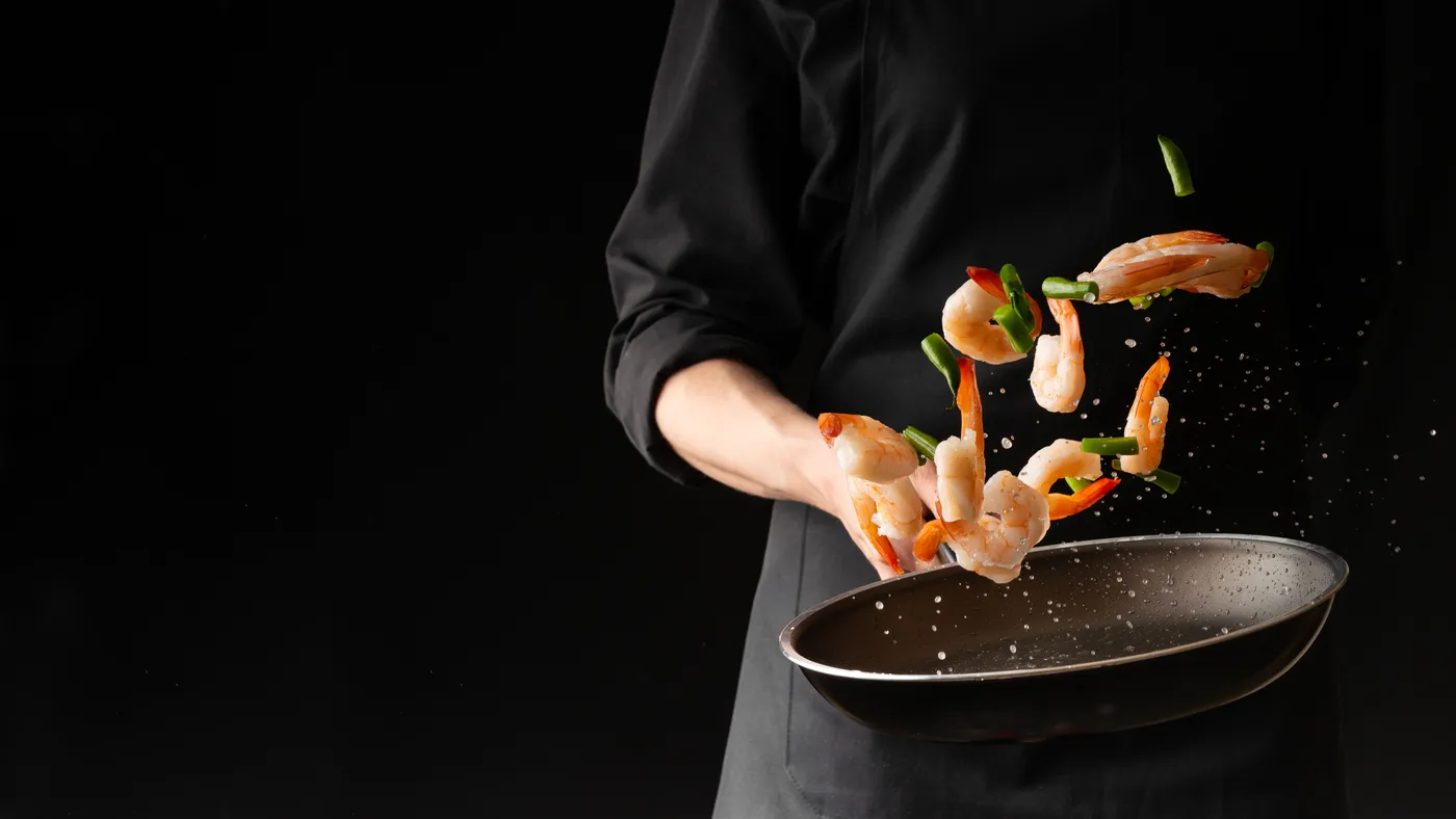 Reinhardt koch - Kochkurse und Gastronomie-Service - Meeresfrüchte, ein Profikoch bereitet Garnelen mit Frühlingsbohnen zu. Zubereitung von Meeresfrüchten, gesunde vegetarische Gerichte und Speisen vor dunklem Hintergrund. Querformat. Orientalische Küche.