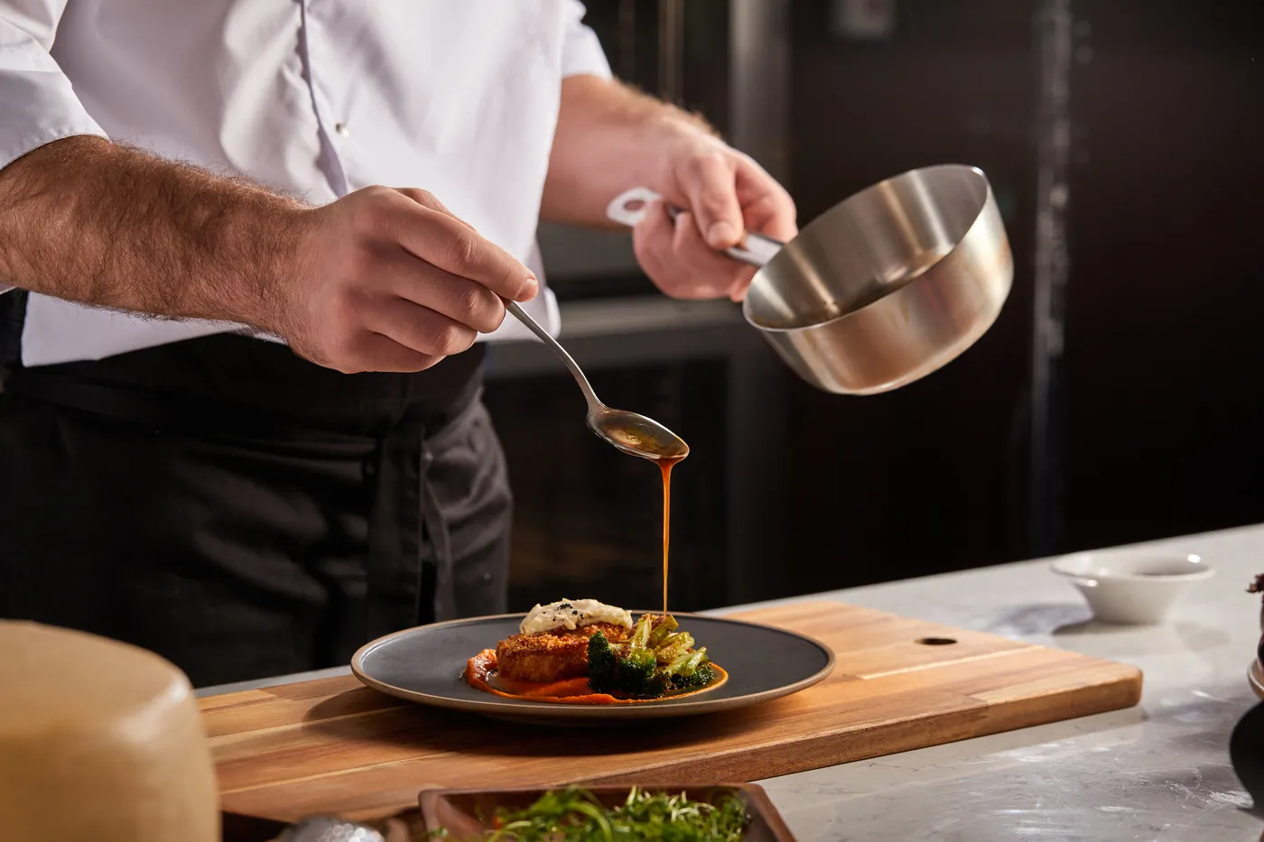 Reinhardt koch - Kochkurse und Gastronomie-Service - Koch mit Schürze gibt Soße auf ein Gericht. Nahaufnahme eines Kochs, der Essen zubereitet, Mahlzeit, in der Küche, Koch beim Kochen, Koch dekoriert Gericht, Nahaufnahme
